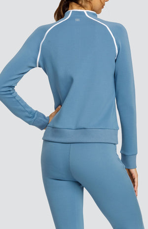 Model wearing a steel blue long sleeve sweatshirt with a quarter zip neckline, white piping accents, and ribbed hem and cuffs. Paired with a matching jogger with welt pockets.