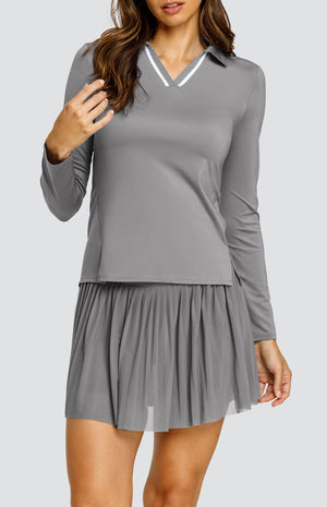 Model wearing a gray long sleeve top with an open v neck foldover collar with white accents and side vents. Paired with a matching mesh pleated skort with solid undershorts.