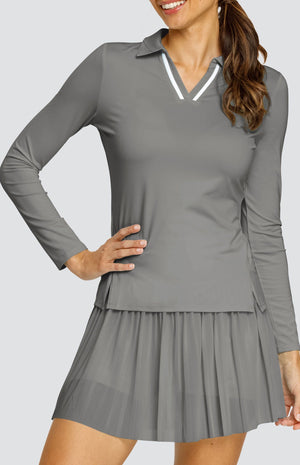 Model wearing a gray long sleeve top with an open v neck foldover collar with white accents and side vents. Paired with a matching mesh pleated skort with solid undershorts.