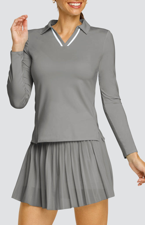 Model wearing a gray long sleeve top with an open v neck foldover collar with white accents and side vents. Paired with a matching mesh pleated skort with solid undershorts.