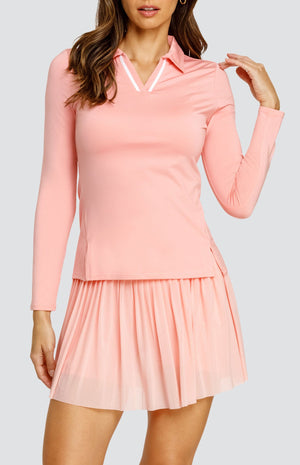 Model wearing a light pink long sleeve top with an open v neck foldover collar with white accents and side vents. Paired with a matching mesh pleated skort with solid undershorts.