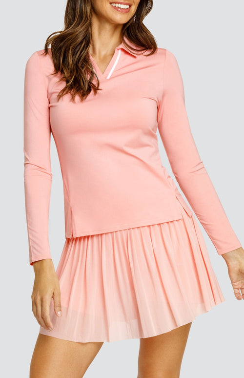 Model wearing a light pink long sleeve top with an open v neck foldover collar with white accents and side vents. Paired with a matching mesh pleated skort with solid undershorts.