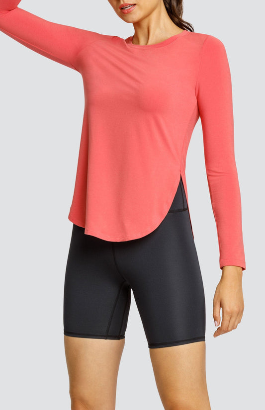 Model wearing a coral long sleeve top with a curved hem and high side slits, and black biker shorts.