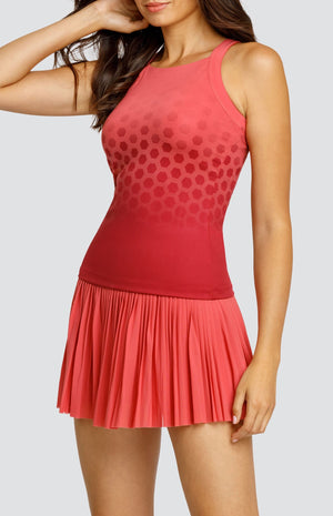 Model wearing a high neck tank top in a coral hexagonal print, and a coral micro pleated skort.