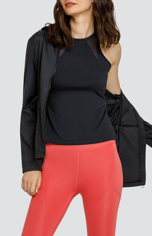 Model wearing a black high neck tank top with mesh inserts, a black hooded zip up jacket with a drawstring waist, and coral high rise leggings with side pockets.