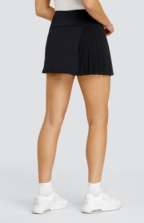 Model wearing a solid black skort with a mesh asymmetrical pleat panel.
