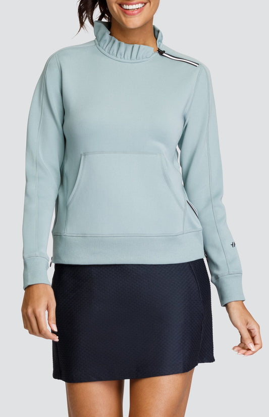 Model is wearing a light Sage Green pullover with a side zipper collar and kangaroo pocket. She is wearing an Onyx textured skort with the pullover. 