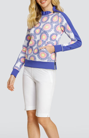 Model wearing a pullover with a ruffle collar in a circular stamp-like pattern with yellow, pink, and blue rings on a white background, with solid white shorts.