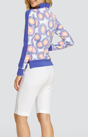 Model wearing a pullover with a ruffle collar in a circular stamp-like pattern with yellow, pink, and blue rings on a white background, with solid white shorts.