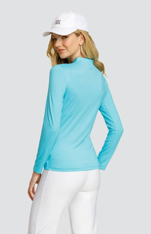 Model wearing a solid turquoise long sleeve top and white pants and a white ball cap.