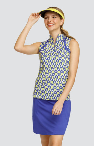 Model wearing a sleeveless golf top with a  teardrop pattern in yellow, blue, and white with blue inserts, a solid blue skort, and a yellow visor.