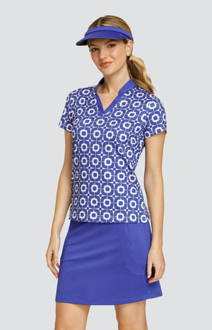 Model wearing a short sleeve golf top with a blue and white geometric pattern, and a solid blue golf skort and visor.