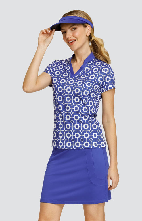 Model wearing a short sleeve golf top with a blue and white geometric pattern, and a solid blue golf skort and visor.