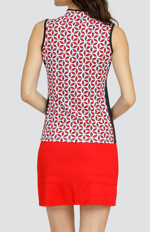 Model wearing a sleeveless golf top with a red and white geometric print, and a red skort.