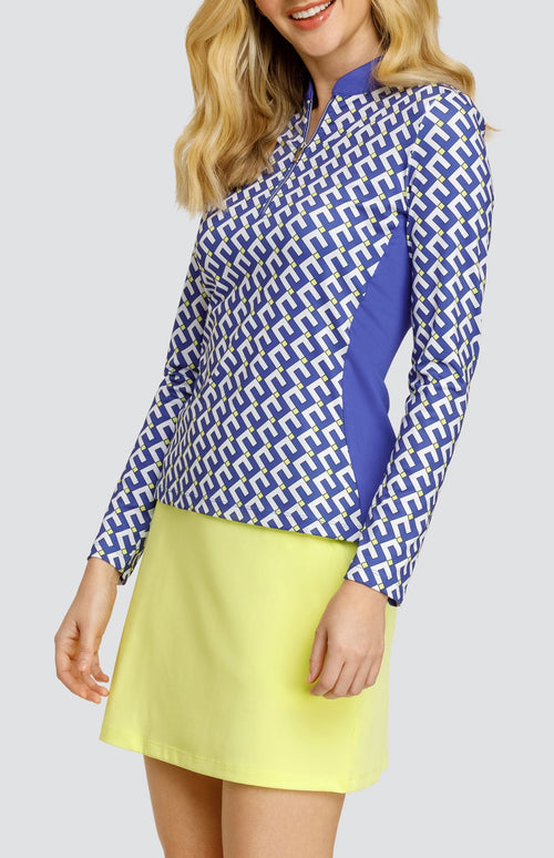 Model wearing a long sleeve golf top with a geometric pattern in blue, white, and yellow with blue side inserts, and a solid yellow pull-on golf skort.