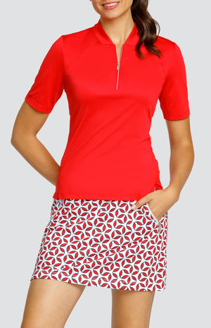 Model wearing a short sleeve red golf top and a skort with a red and white geometric print.