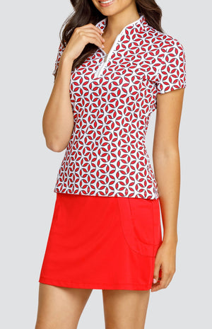 Model wearing a short sleeve golf top with a red and white geometric print, and a solid red skort.