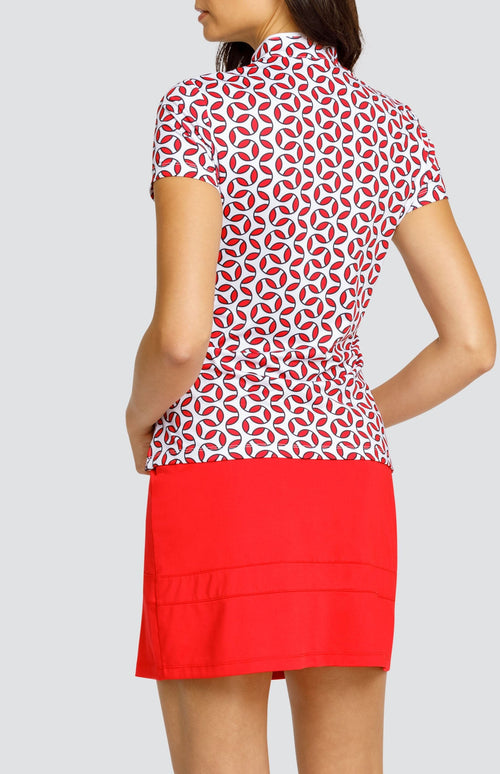 Model wearing a short sleeve golf top with a red and white geometric print, and a solid red skort.