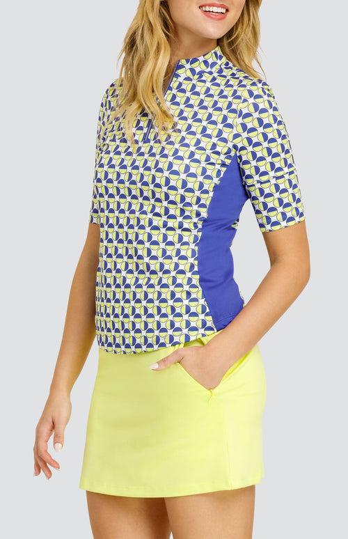 Model wearing an elbow sleeve golf top with a geometric circular pattern in blue and yellow on a white background, and a solid yellow pull-on golf skort.