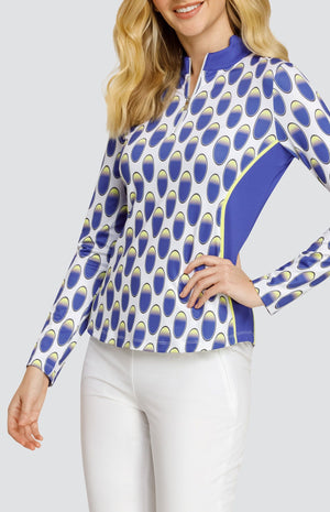 Model wearing a long sleeve golf top with an oval pattern in blue and yellow on a white background, and solid white pull on golf pants.