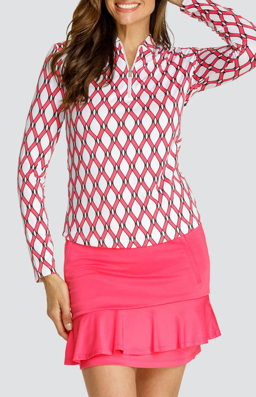 Model wearing a long sleeve quarter-zip golf top with a pink and white lattice pattern and a pull on pink golf skort with a flounce insert.