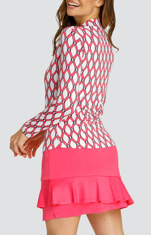 Model wearing a long sleeve quarter-zip golf top with a pink and white lattice pattern and a pull on pink golf skort with a flounce insert.