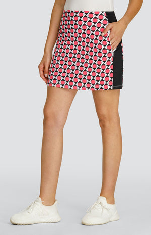 Model wearing a pull on golf skort with a pink, black, and white geometric pattern and black side inserts.