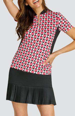 Model wearing a short sleeve quarter-zip golf top with a pink, white and black geometric pattern and black inserts, with a black pleated golf skort.