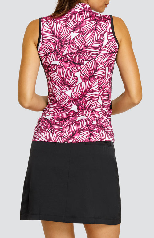 Model wearing a sleeveless quarter-zip golf top in a pink frond print on a white background with black side inserts, paired with a solid black zip and hook closure golf skort.