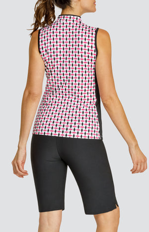 Model wearing a sleeveless quarter-zip golf top in a pink and black geometric alternating diamond print on a white background with black side inserts, paired with solid black pull-on golf shorts.