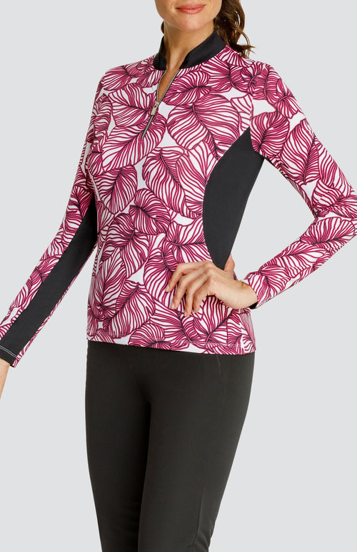 Model wearing a long sleeve quarter-zip golf top in a pink frond print on a white background with black side and underarm inserts, paired with a solid black pull-on golf pant.