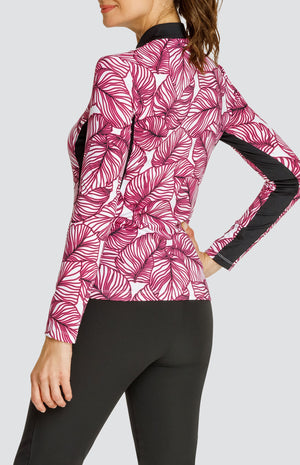 Model wearing a long sleeve quarter-zip golf top in a pink frond print on a white background with black side and underarm inserts, paired with a solid black pull-on golf pant.