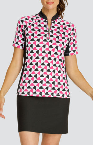 Model wearing a short sleeve quarter-zip golf top in a pink and black alternating triangular print on a white background with black side and underarm inserts, paired with a solid black pull-on golf skort.