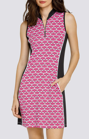 Model wearing a sleeveless quarter-zip golf dress in a pink geometric floral print on a white background with black side inserts.