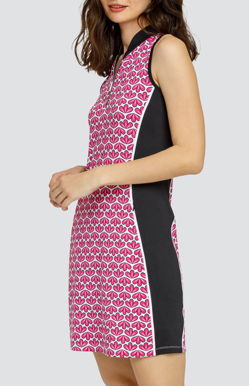 Model wearing a sleeveless quarter-zip golf dress in a pink geometric floral print on a white background with black side inserts.