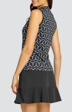 Model wearing a sleeveless golf top with a black and white geometric pattern and a black skort.