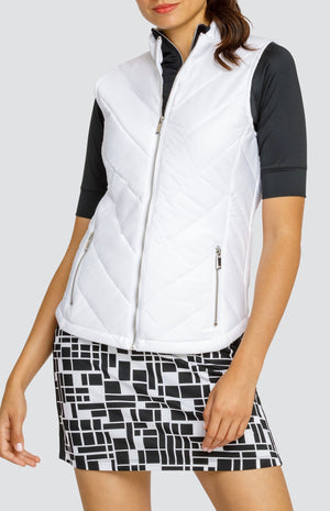 Model wearing a short sleeve black golf top and a black and white geometric printed skort, and a sleeveless puffer vest in white.