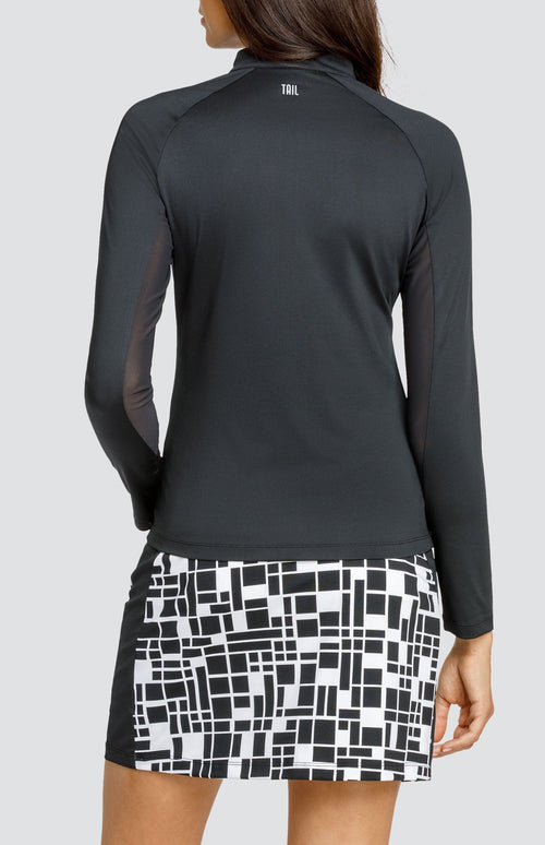 Model wearing a black raglan long sleeve golf top and a skort with a geometric black and white print.