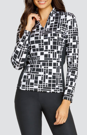 Model wearing an open V-neck golf top with long sleeves in a black and white geometric print with black side inserts.