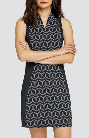 Model wearing a sleeveless golf dress with a black and white geometric print with alternating three-point shapes and black side inserts