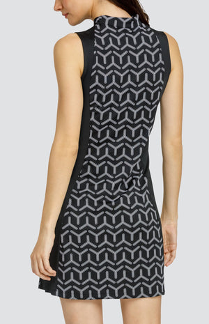 Model wearing a sleeveless golf dress with a black and white geometric print with alternating three-point shapes and black side inserts