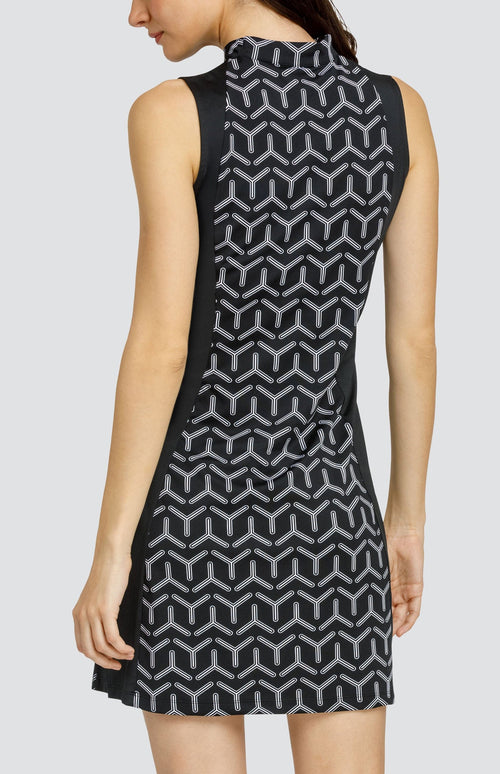 Model wearing a sleeveless golf dress with a black and white geometric print with alternating three-point shapes and black side inserts